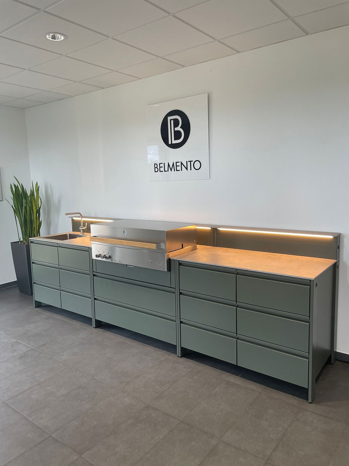 Belmento Outdoorküche mit Grill, Spüle und Schubladenmodulen in moderner Ausstellung mit indirekter Beleuchtung und Logo an der Wand