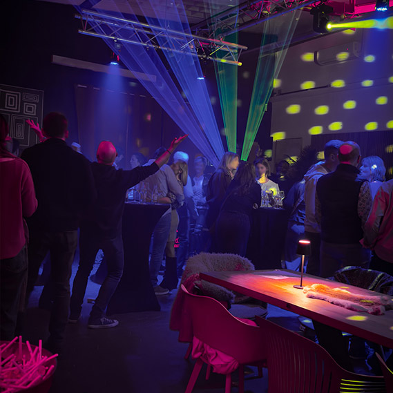 Besucher auf einer Afterwork-Party in unserer Eventlocation mit DJ-Musik, Lichtshow und entspannter Networking-Atmosphäre zwischen Stehtischen und Lounge-Bereich
