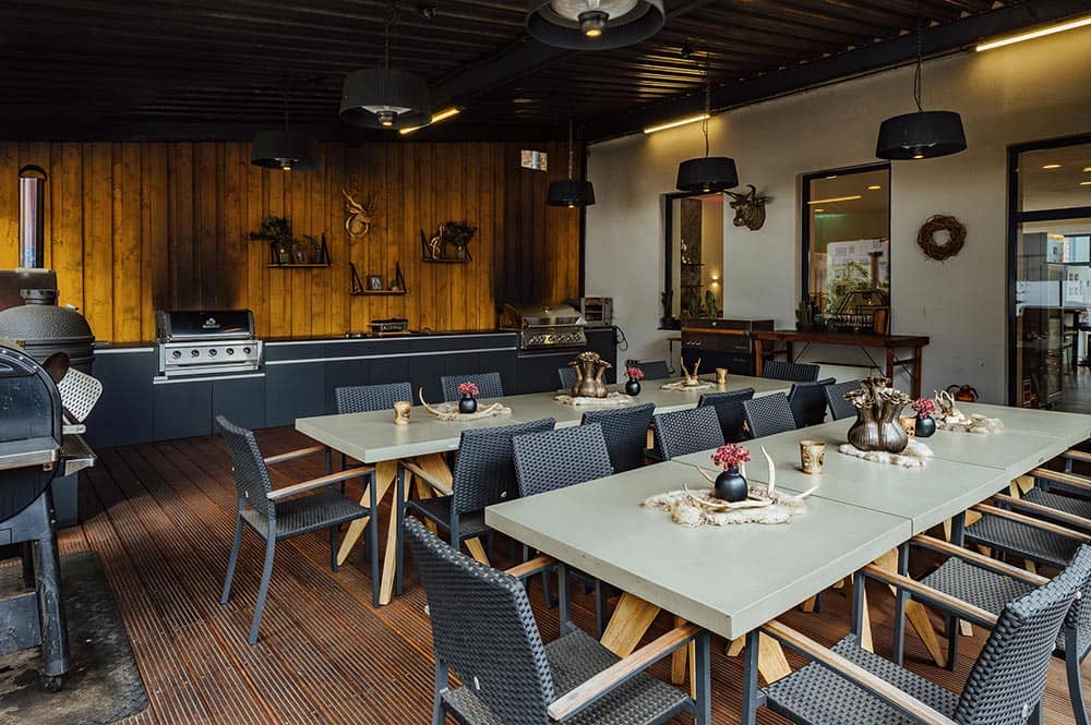 Gemütlicher, überdachter Außenbereich mit Grill und rustikal dekorierten Tischen vor Halle 22 im Grillfachgeschäft Düsseldorf